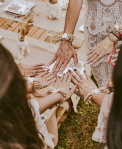 Women at a bridal shower or bachelorette party stretching their hands out together in a ring. They have TEAM BRIDE written on the back of their hands. Dressed in white dresses and beautiful jewelry they are ready for some bridal shower games!
